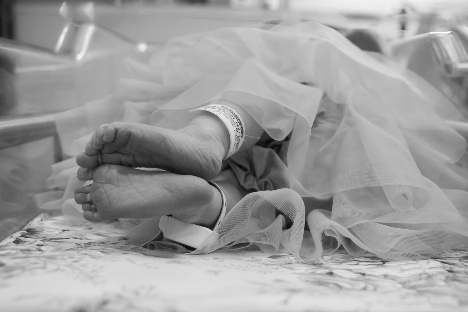 Black and white close-up of a newborns feet with hospital ID bands wrapped in soft tulle fabric.