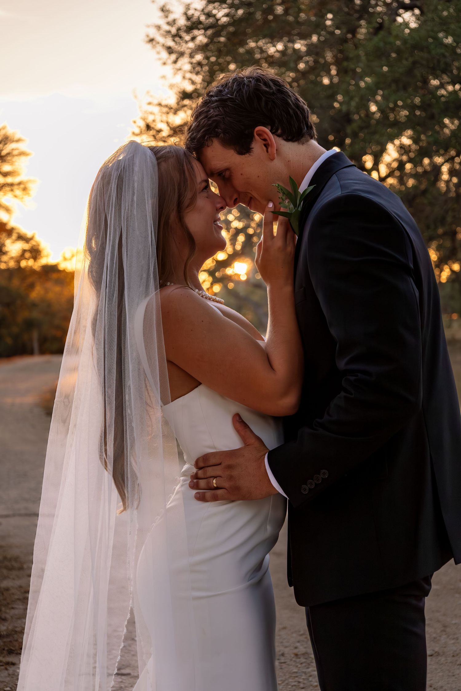 Bride and groom sharing a romantic moment under a veil during a golden sunset outdoors.