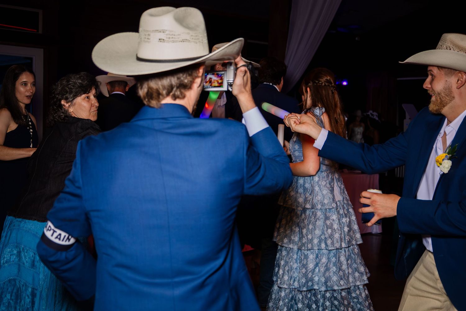 People in blue suits and cowboy hats dancing at a lively indoor event or wedding reception.