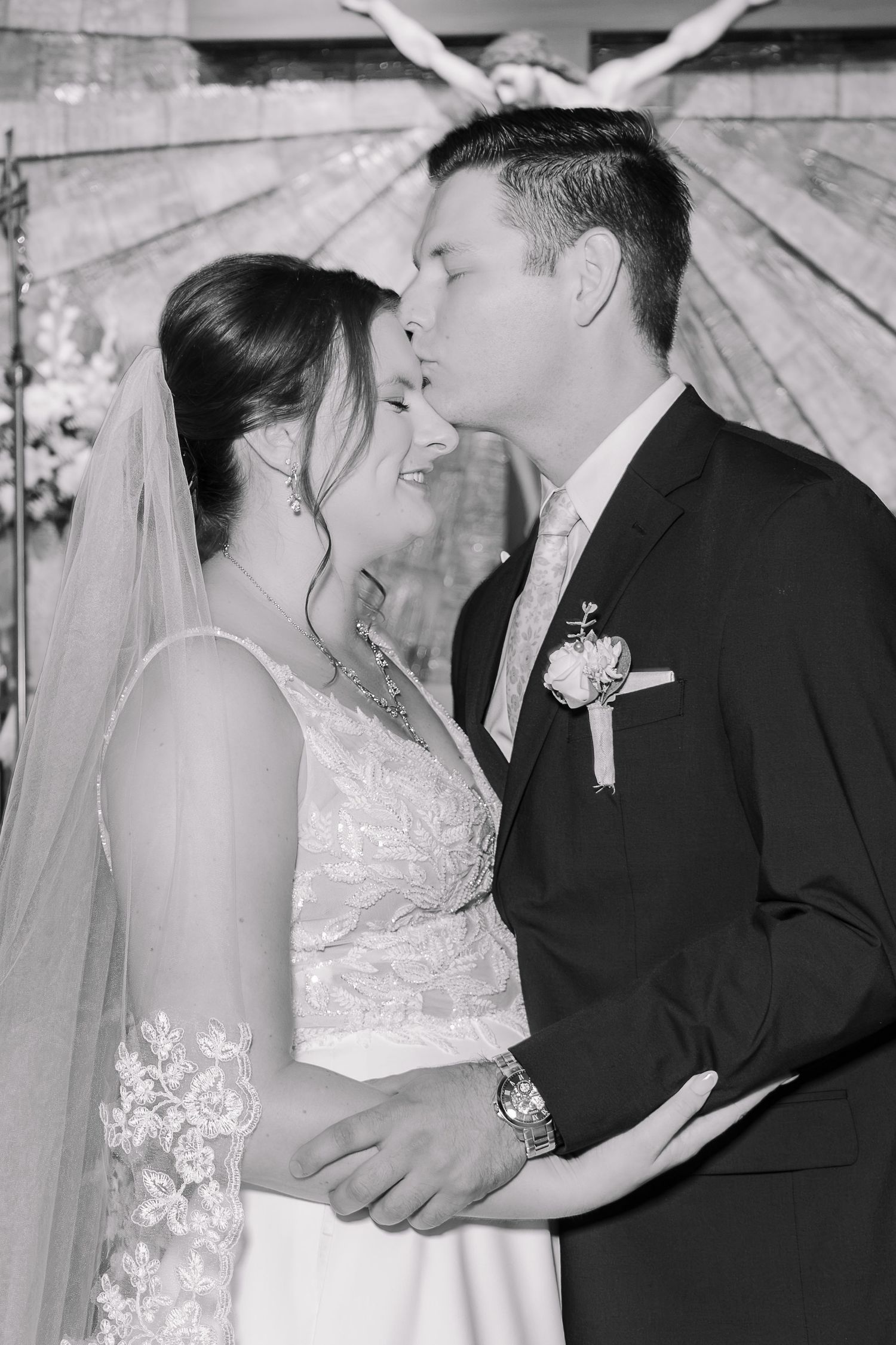 Black and white wedding photo of bride and groom sharing a romantic moment at the altar.