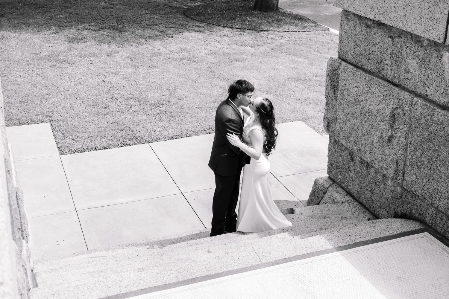 Black and white aerial view of a bride and groom sharing a romantic moment on stone steps.