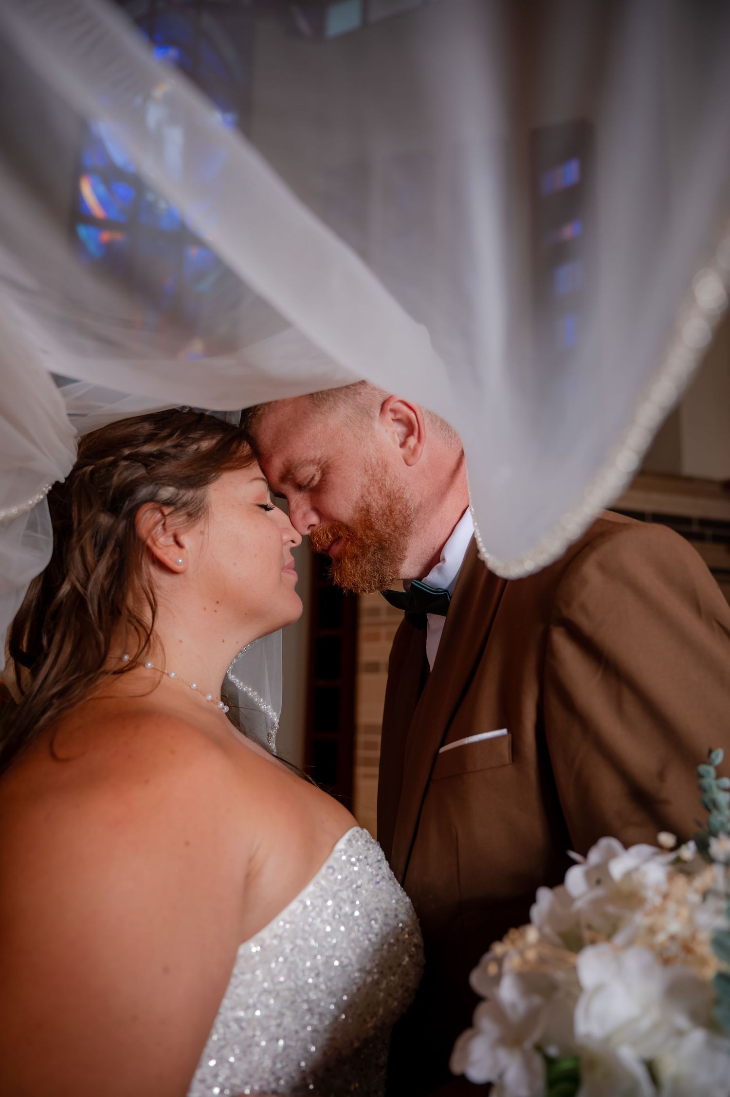 Bride and groom sharing an intimate moment under a flowing veil at their wedding ceremony.