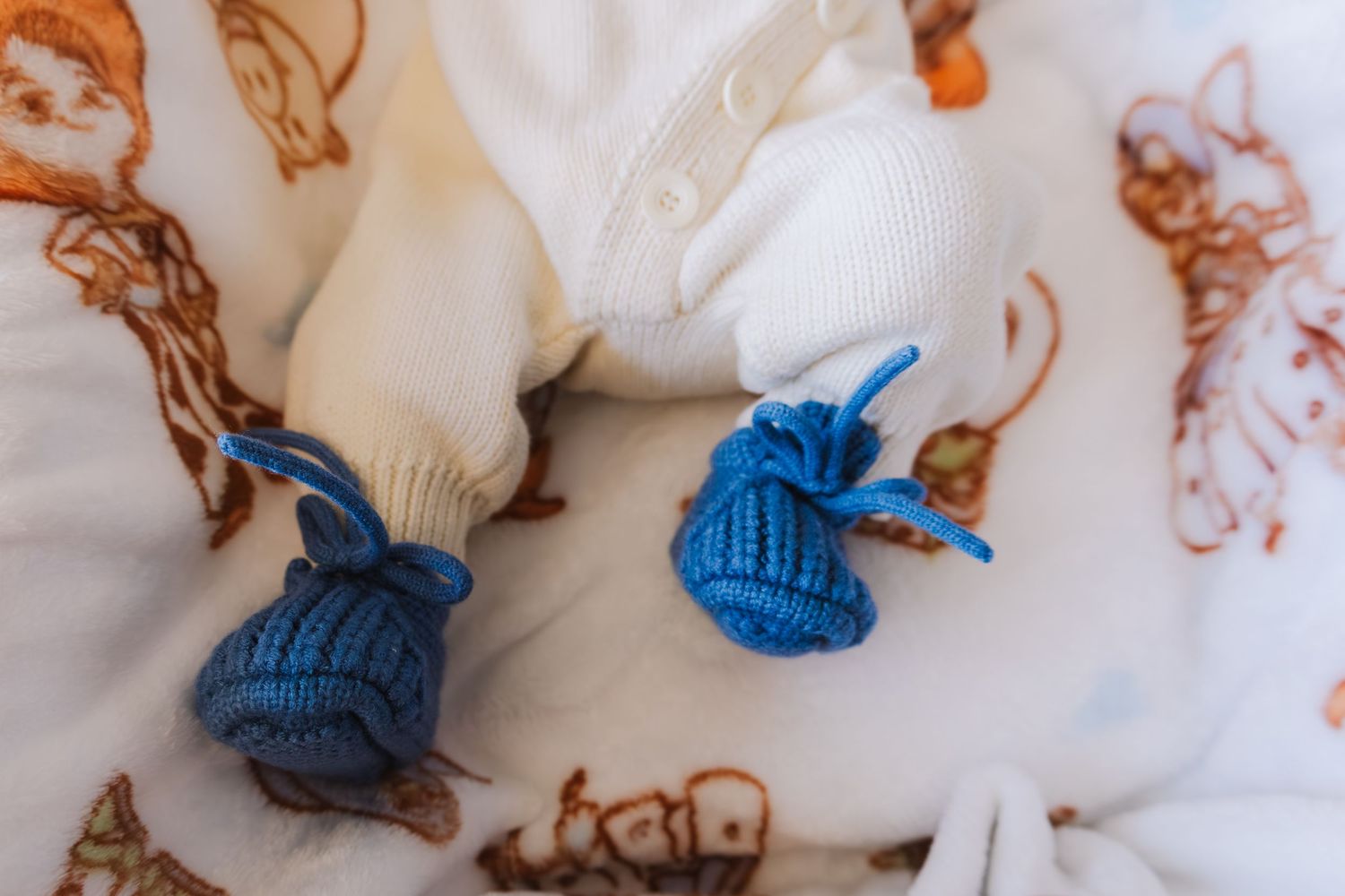 Tiny blue knitted baby booties resting on a white newborn blanket with illustrations.
