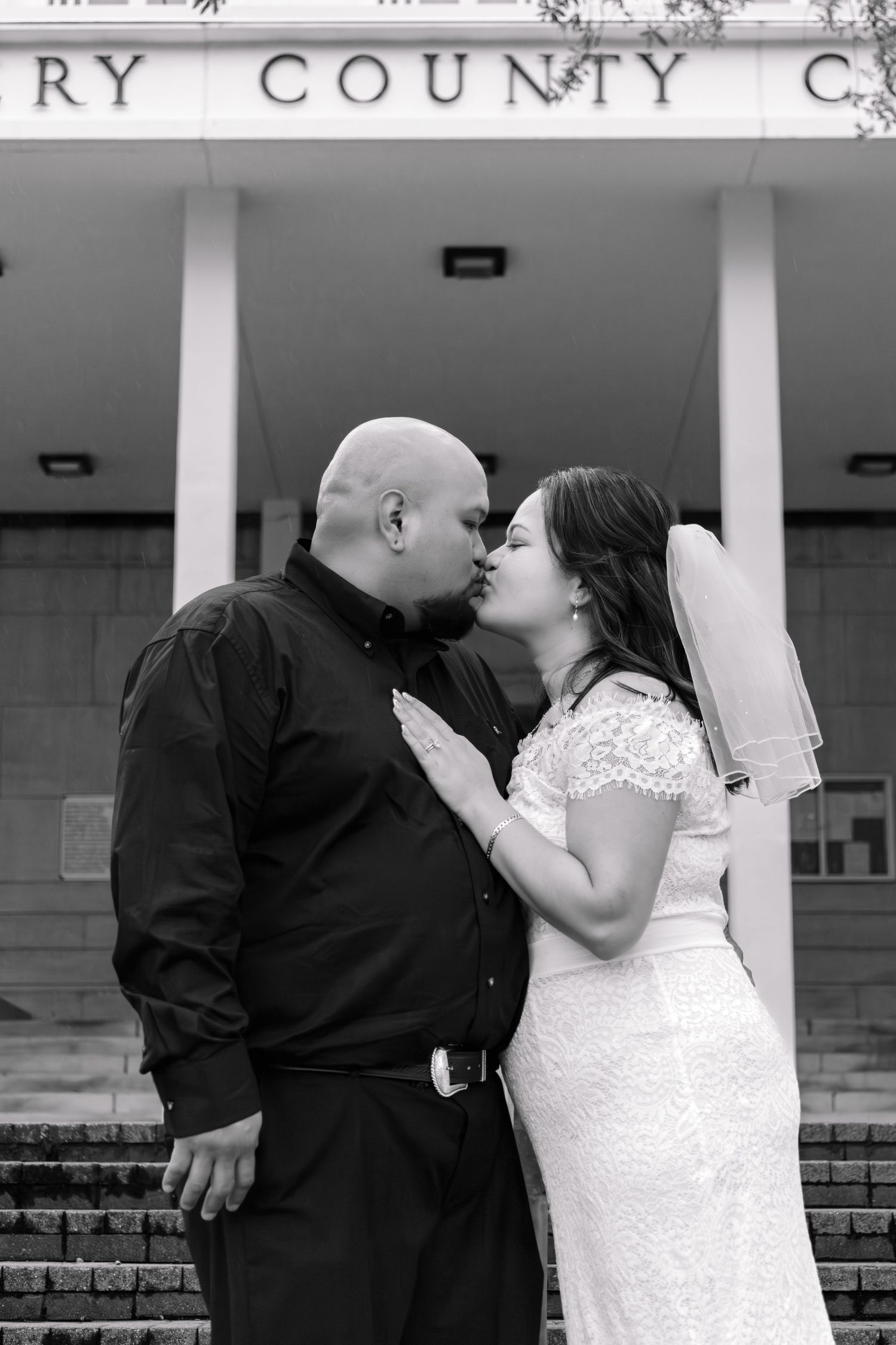 Bride and groom sharing a kiss in front of a county courthouse in black and white.