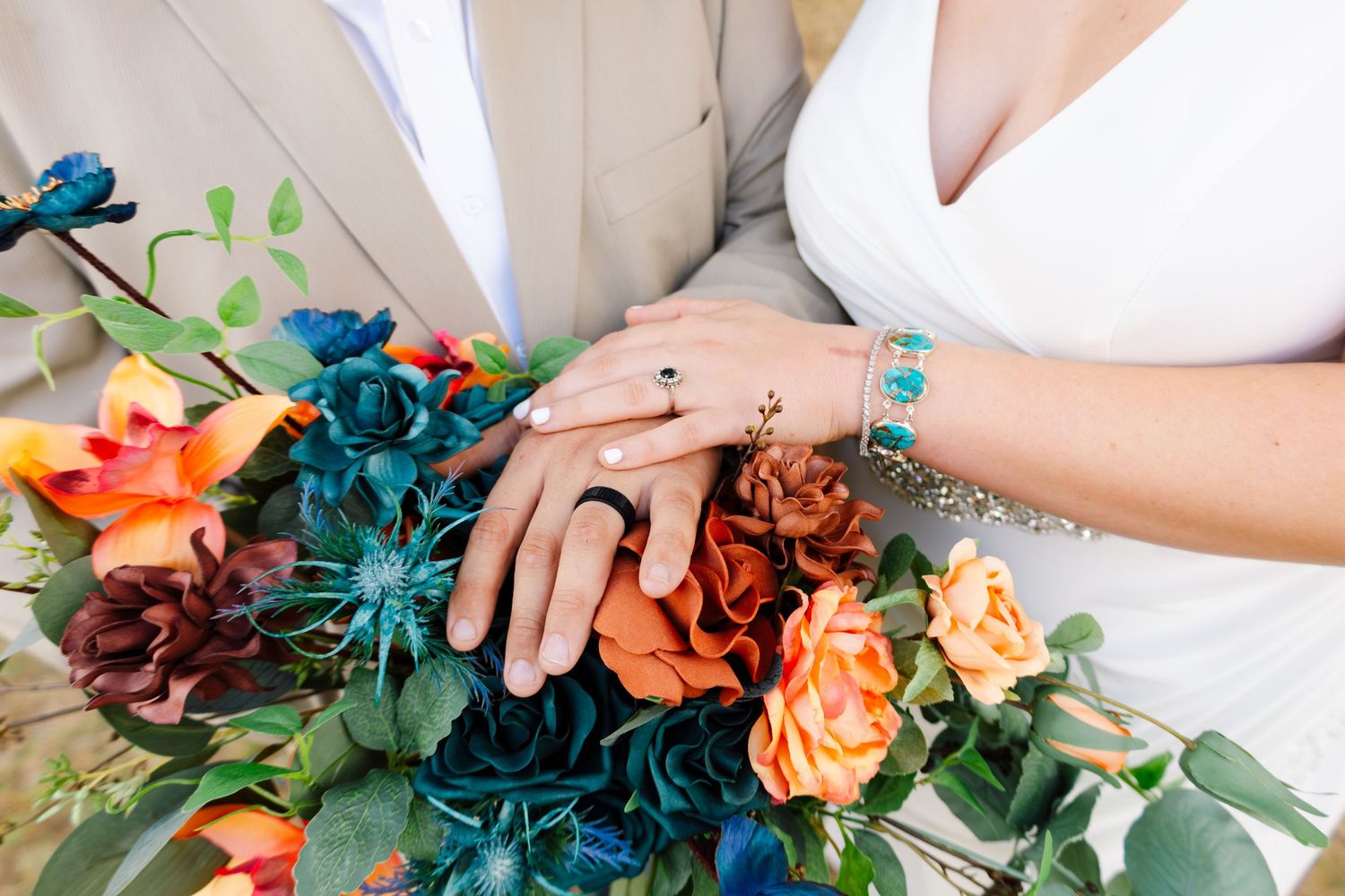 Close-up of bride and groom hands with rings over vibrant colorful bouquet.