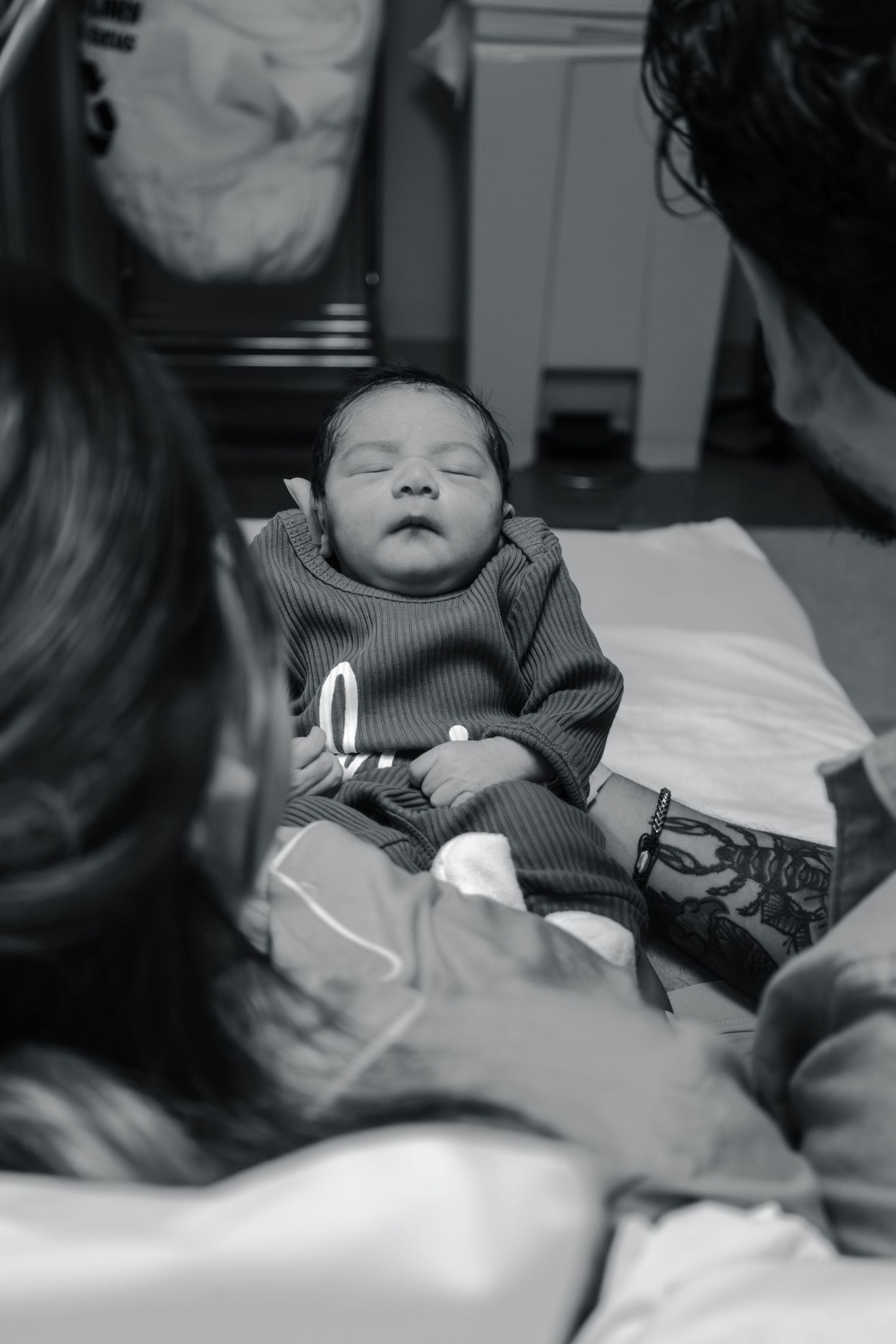 Black and white photo of a peaceful newborn baby in striped outfit lying on a blanket.