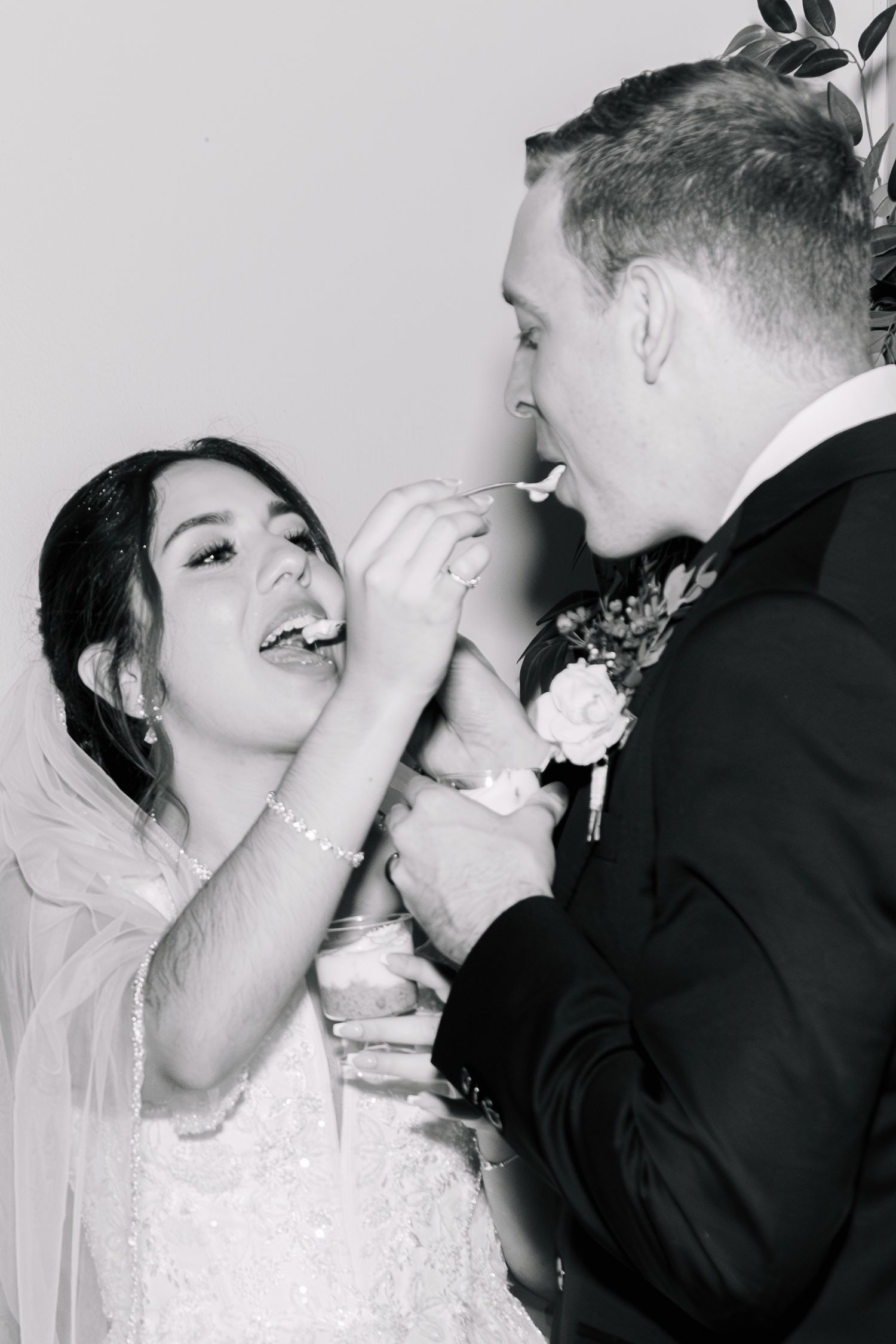Black and white photo of bride and groom sharing wedding cake at reception.