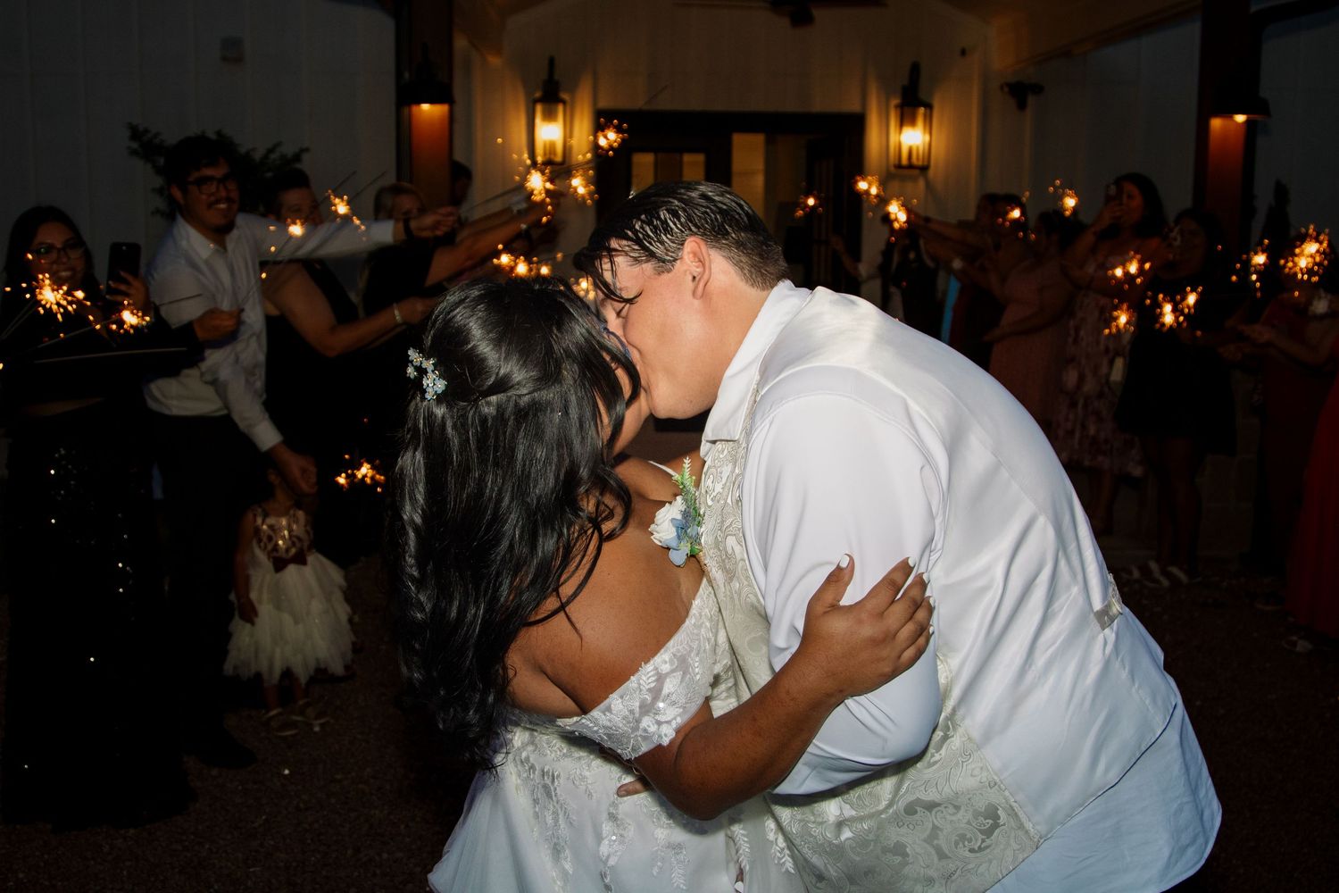 Bride and groom sharing a kiss surrounded by sparkler-holding guests at a wedding reception.