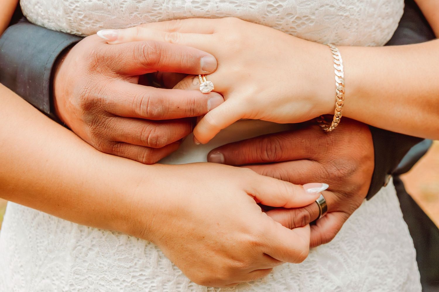 Close-up of a couple's hands intertwined showing diamond engagement ring and gold bracelet.