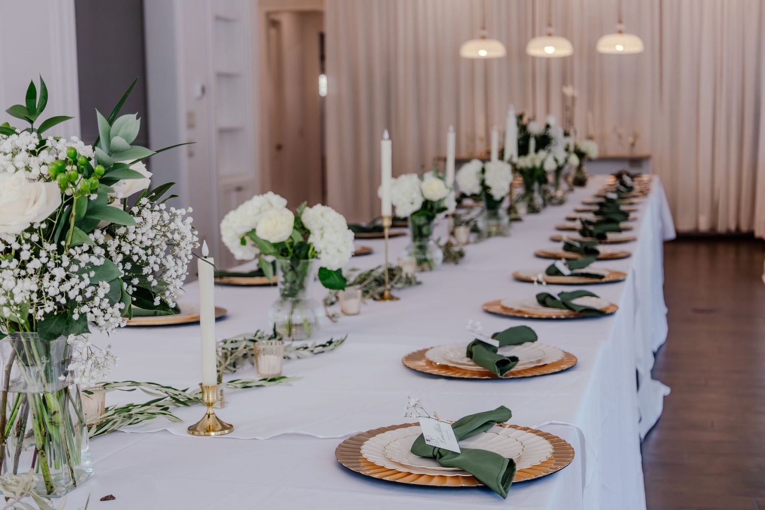 Elegant wedding reception table with white florals, candles, and gold charger plates.