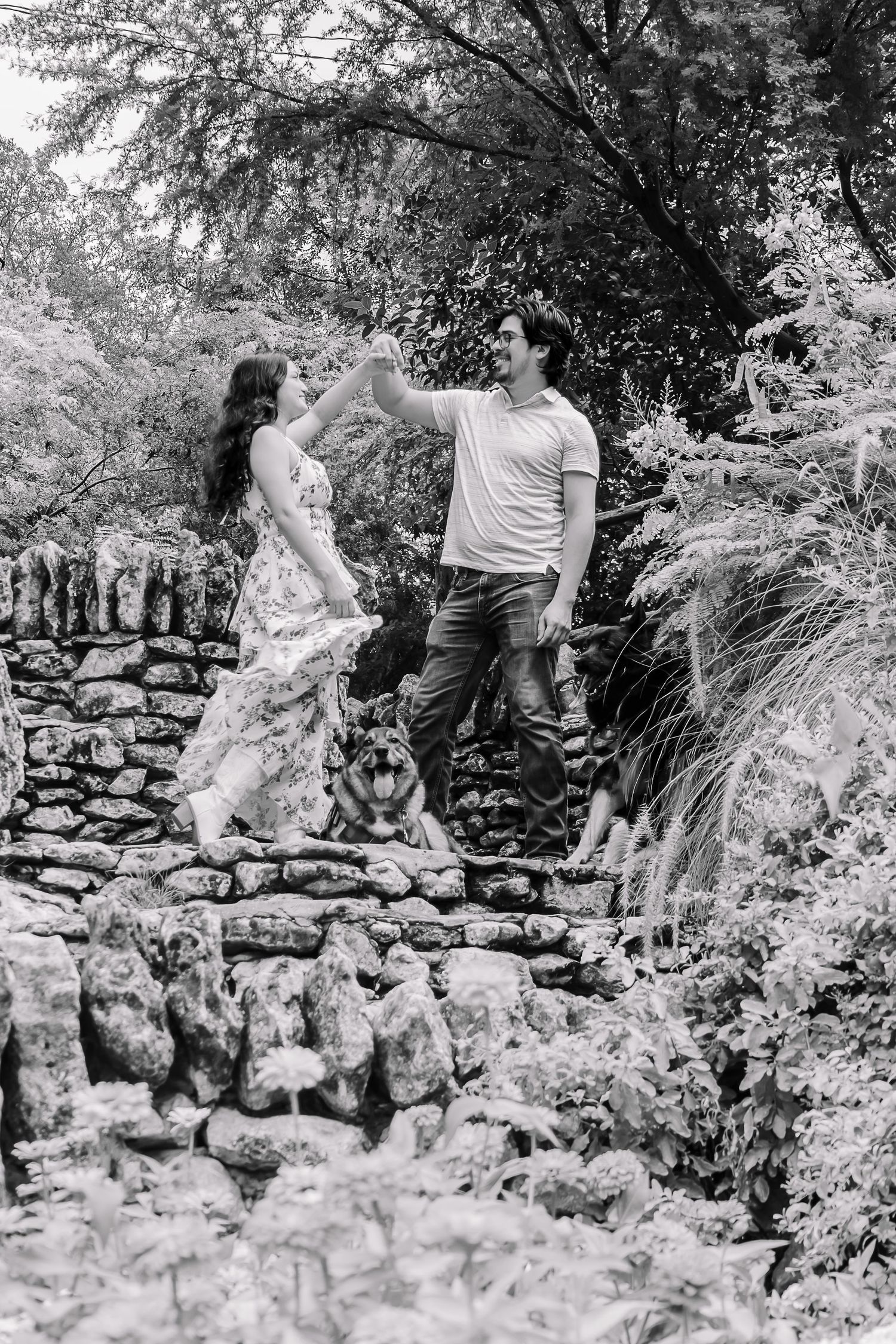 Black and white photo of a couple dancing on stone steps in a lush garden with a dog nearby.