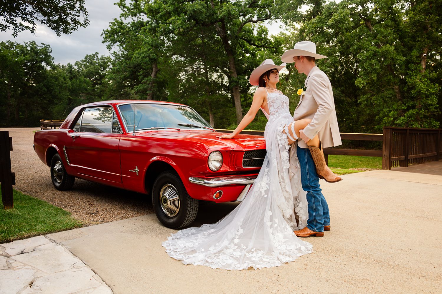 Bride and groom in cowboy hats pose beside a classic red Ford Mustang on their rustic Texas wedding day.