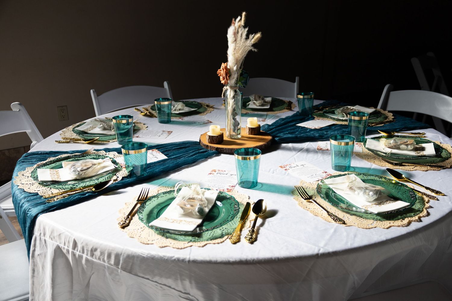 Round wedding reception table set with teal velvet runner, gold chargers, and teal glassware.