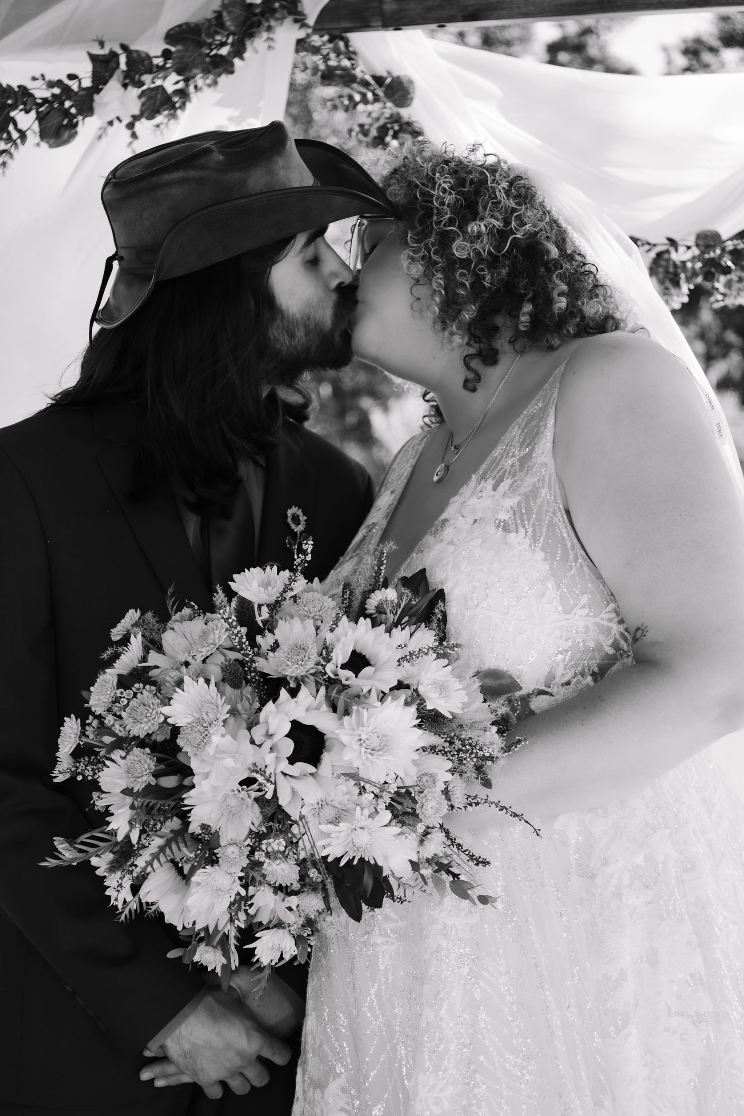 Black and white photo of bride and groom kissing under veil with bouquet.