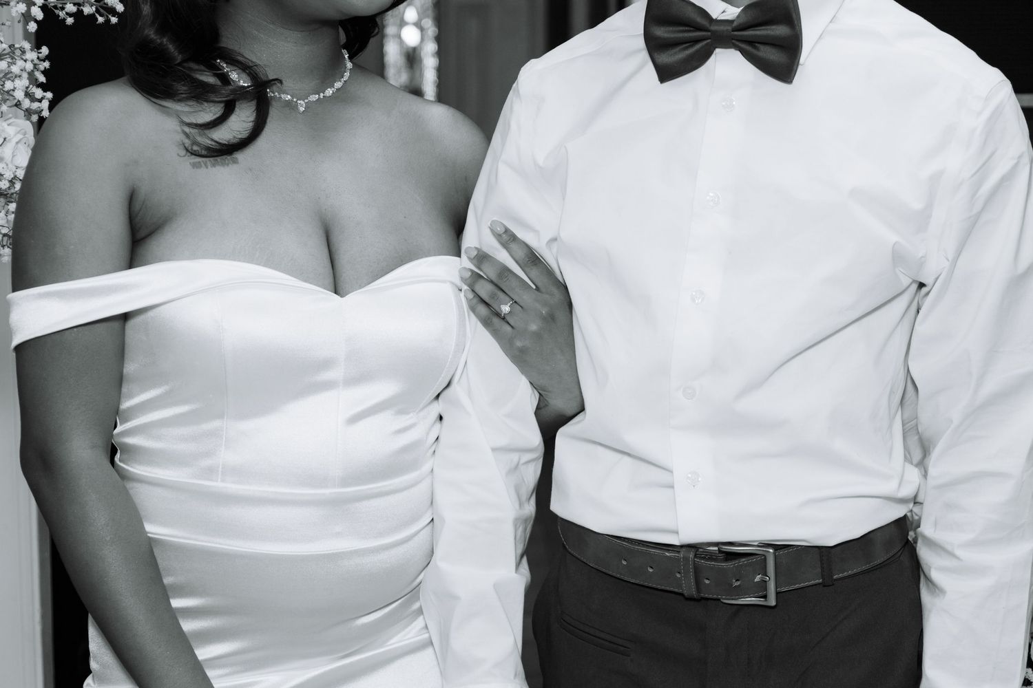 Black and white close-up of bride in off-shoulder gown and groom in white shirt with black bow tie.