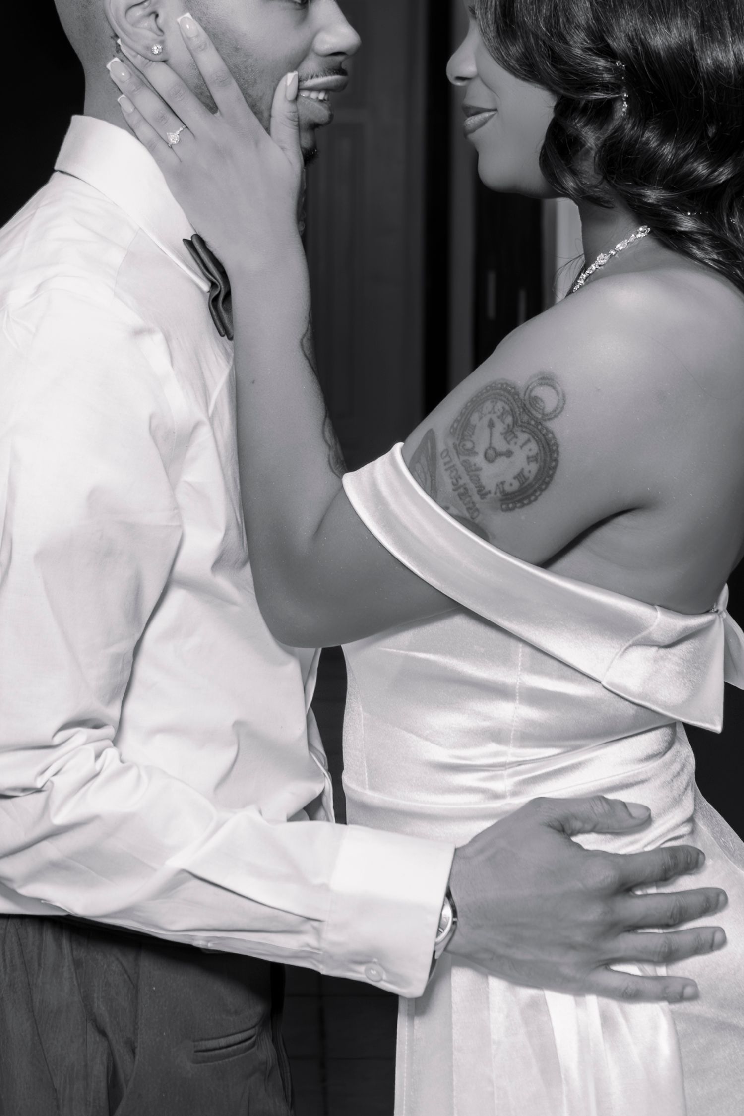 Black and white close-up of a bride and groom embracing, showcasing bride's shoulder tattoo.