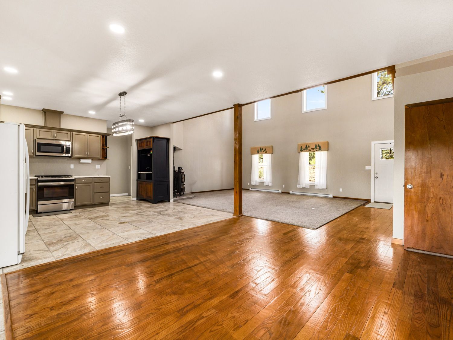 Open concept kitchen and living area with hardwood floors, stainless steel appliances, and high ceilings.