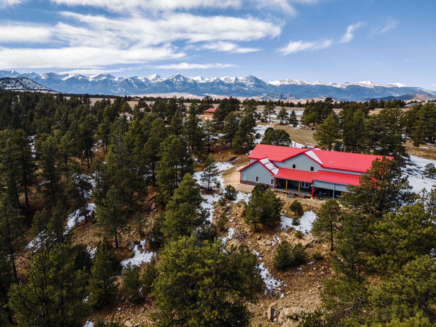 Mountain property aerial view showing red-roofed structures amid winter forest landscape.