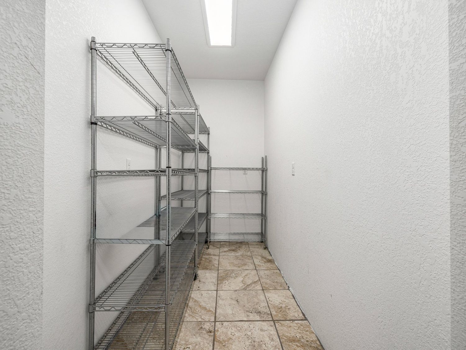 Narrow storage room with metal wire shelving units and tile flooring in a textured white wall space.