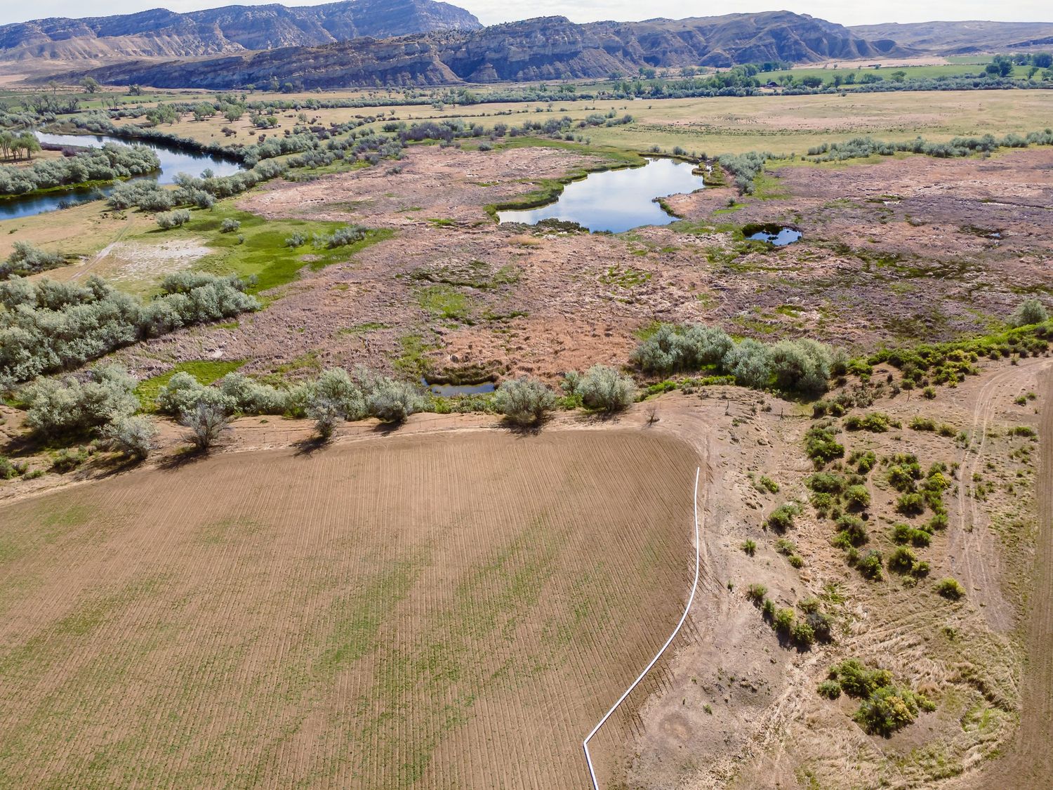 Aerial view of rural farmland with ponds, wetlands, and red rock mountains in a scenic western landscape.