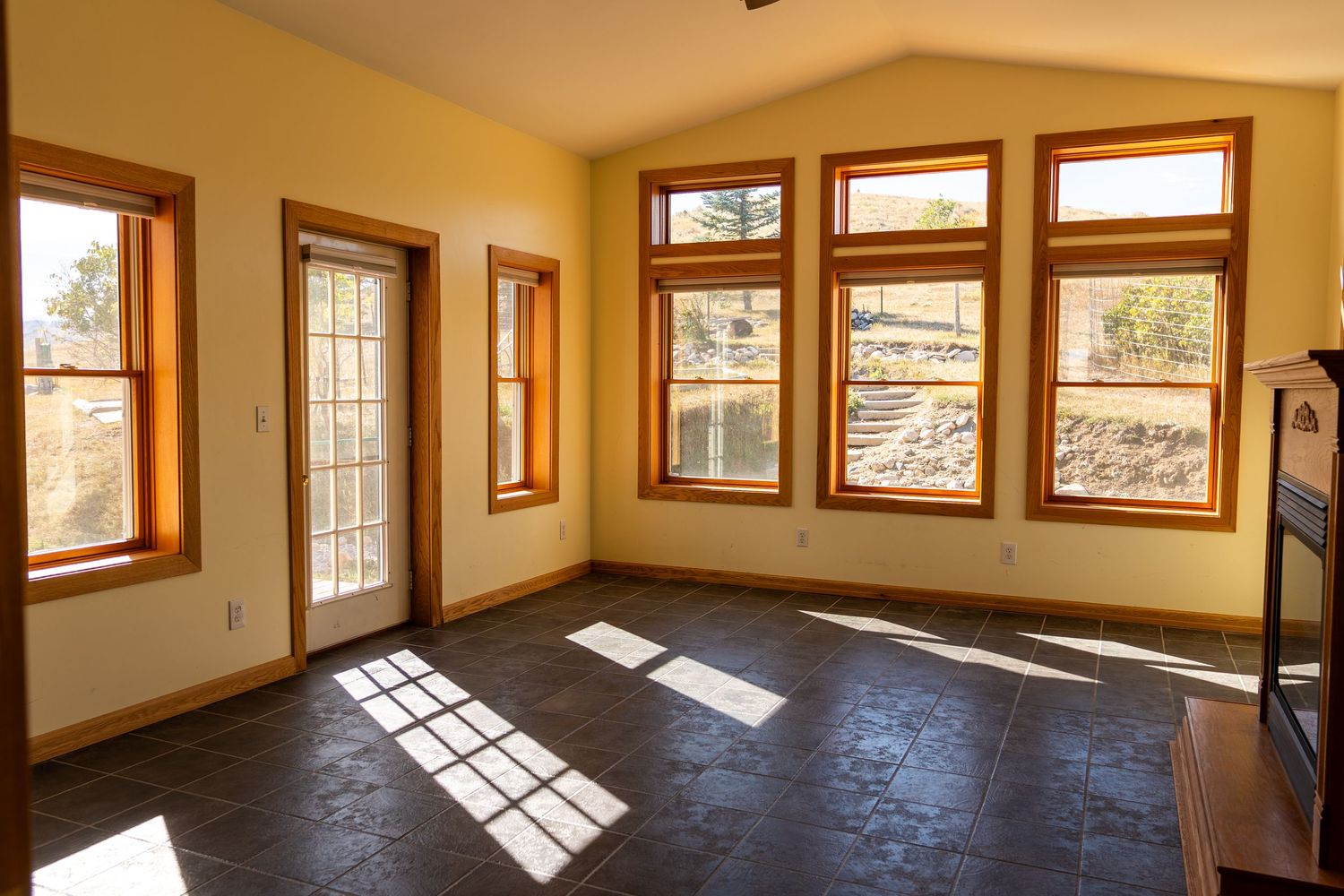 Bright sunroom with dark tile floors, wood-trimmed windows, and vaulted ceiling in a modern home.