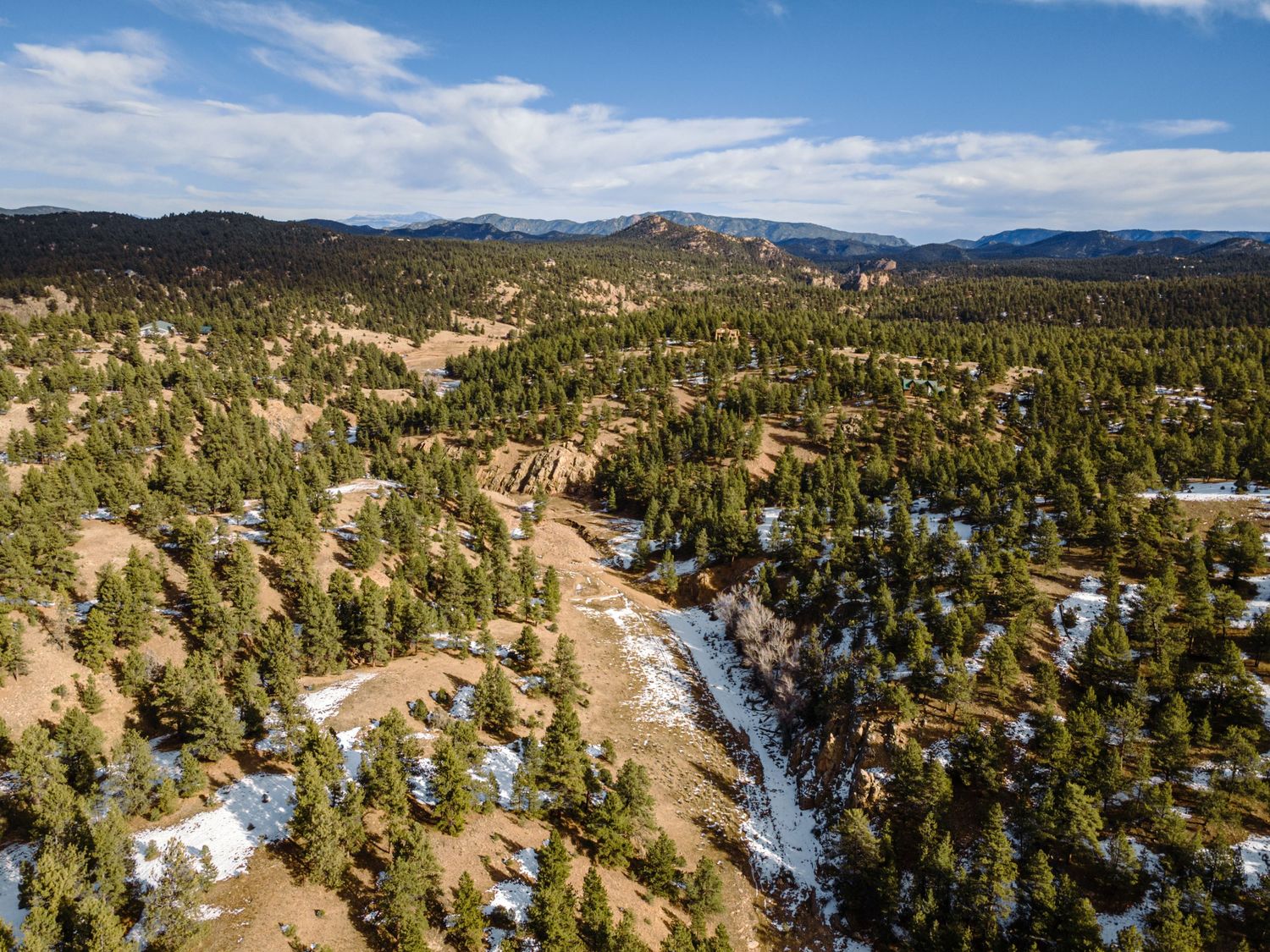 Panoramic view of winding mountain roads through pine forest with patches of snow.