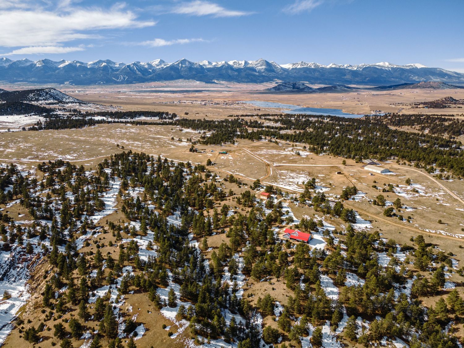 Aerial view of snowy mountain landscape with scattered homes and pine trees in a rural valley setting.