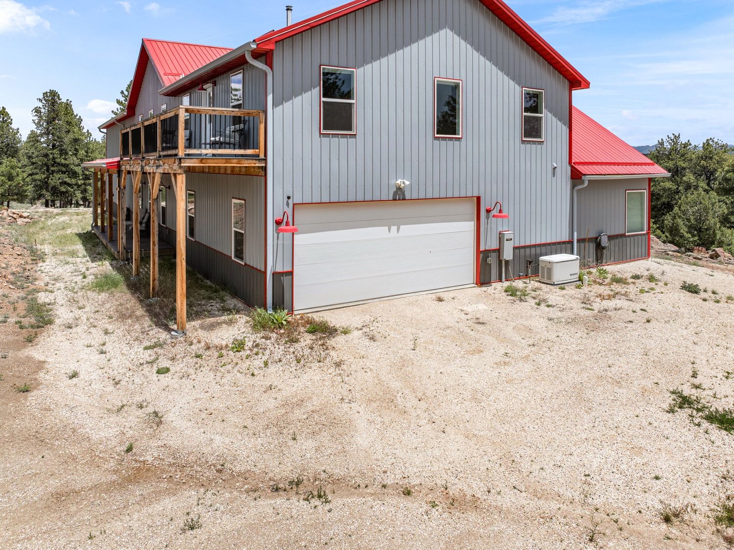 Two-story home with red metal roof, gray siding, attached garage, and deck overlooking a rural landscape.
