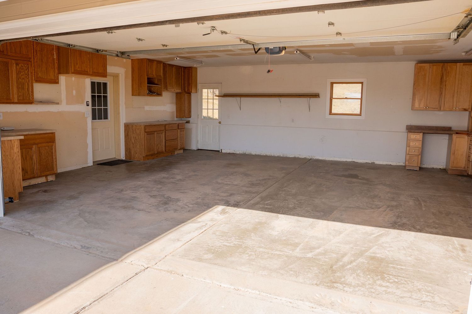 Spacious empty garage interior with wooden cabinets, concrete floor, and natural light from windows.