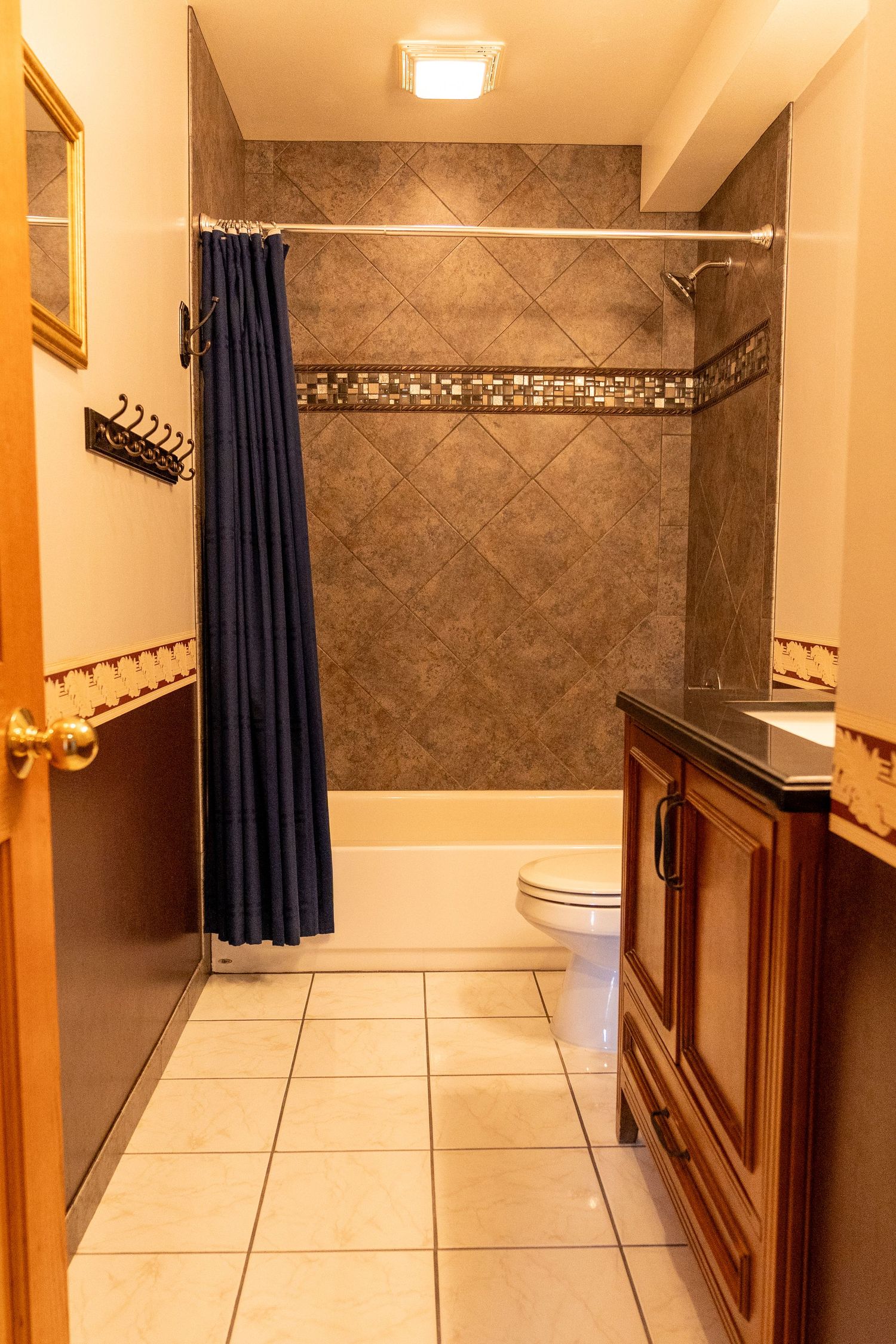 Bathroom with blue shower curtain, diagonal tile surround, white toilet, wood vanity, and light tile floor.