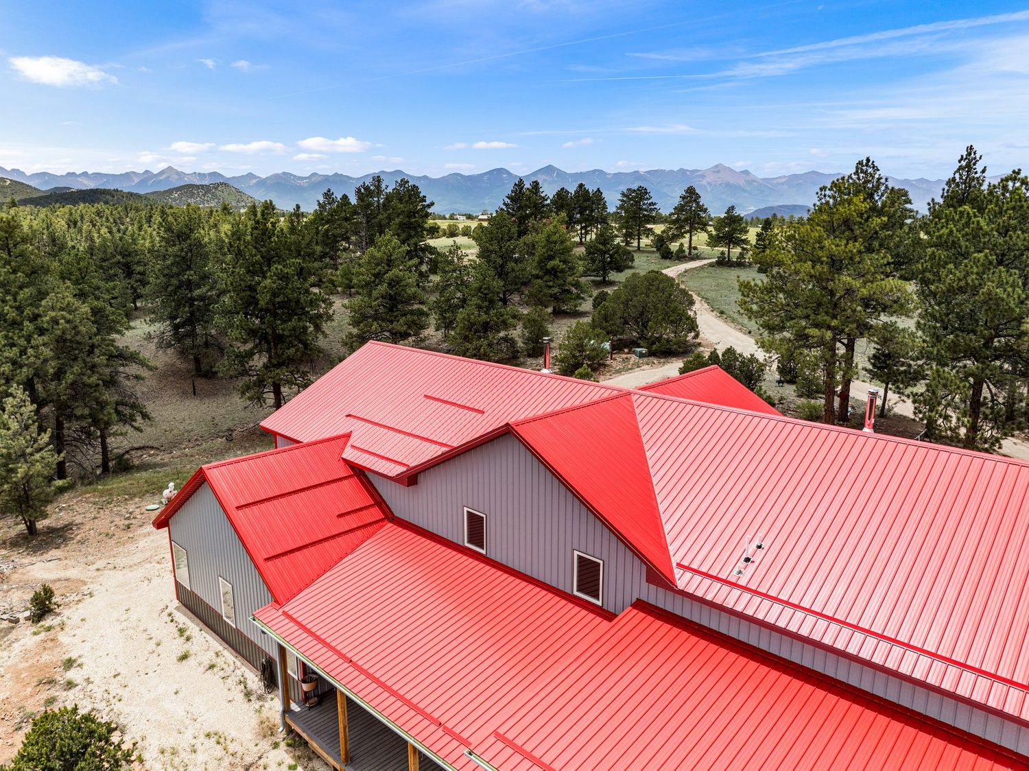 Aerial view of large home with red metal roof surrounded by pine trees and mountain views.