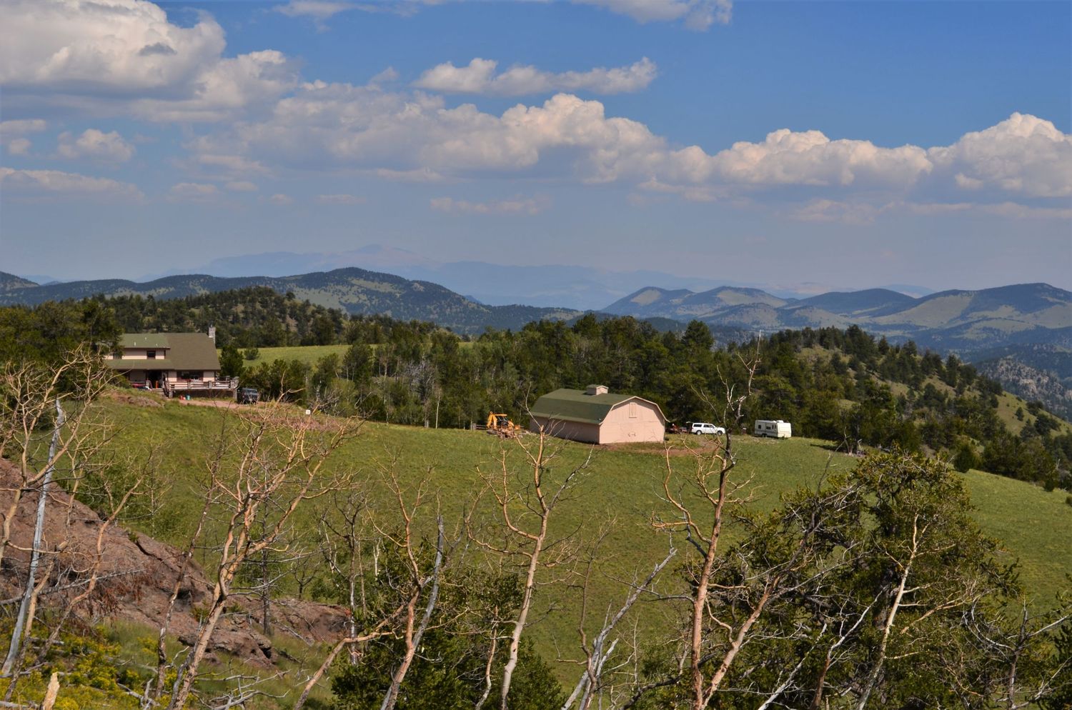 Scenic mountain landscape with green hills and pretty farm buildings under a blue sky with clouds.
