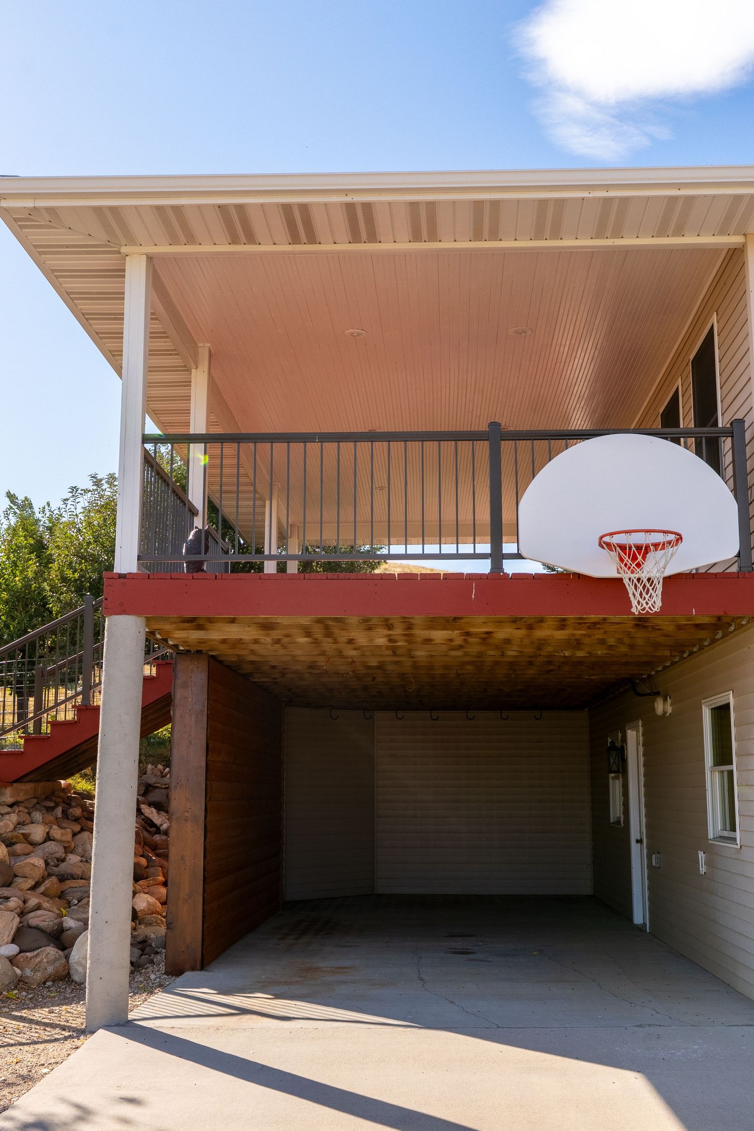 House exterior with basketball hoop mounted under upper deck balcony above garage door on concrete driveway.