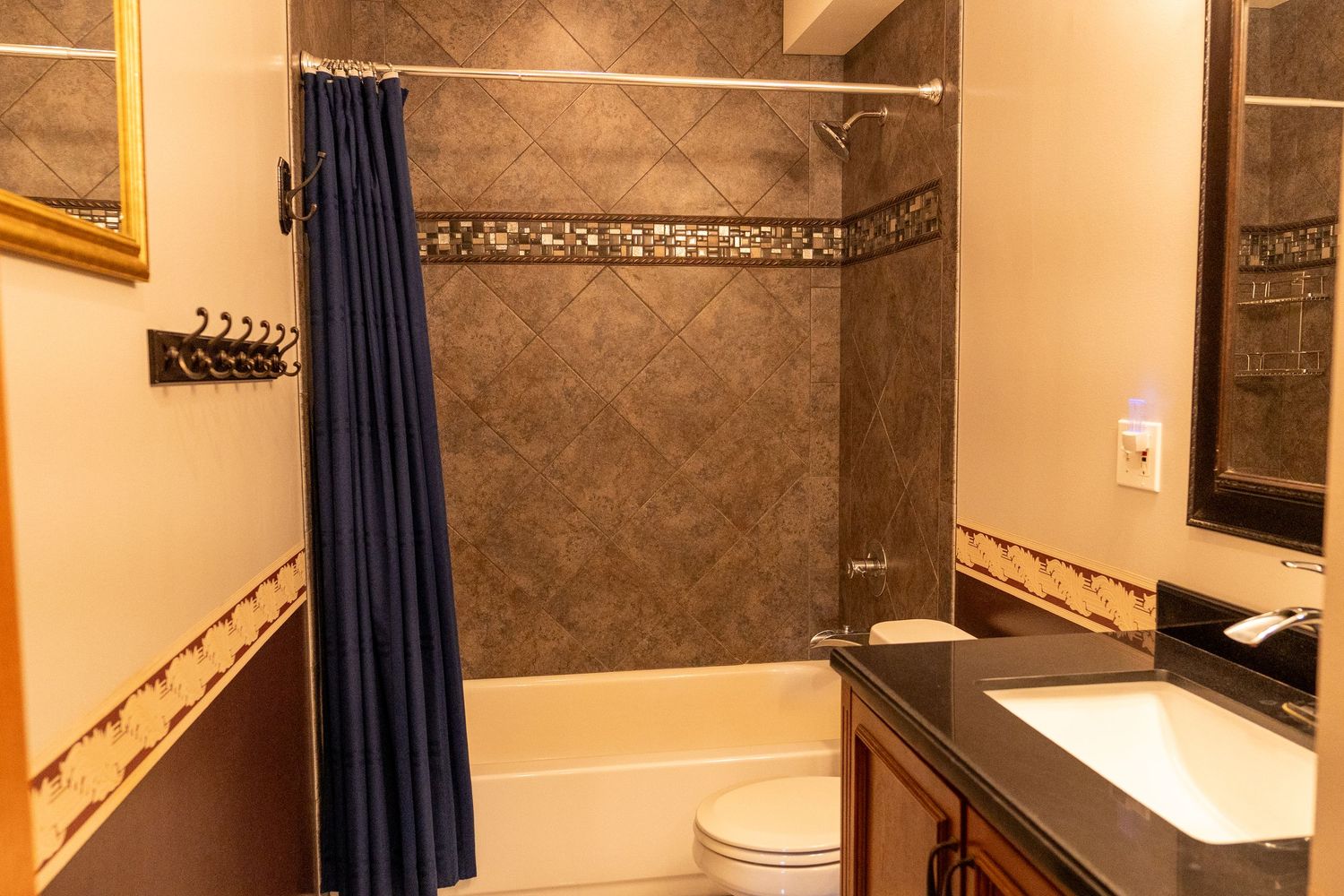 Modern bathroom with dark tile shower, blue curtain, white toilet, and granite vanity sink with warm beige walls.