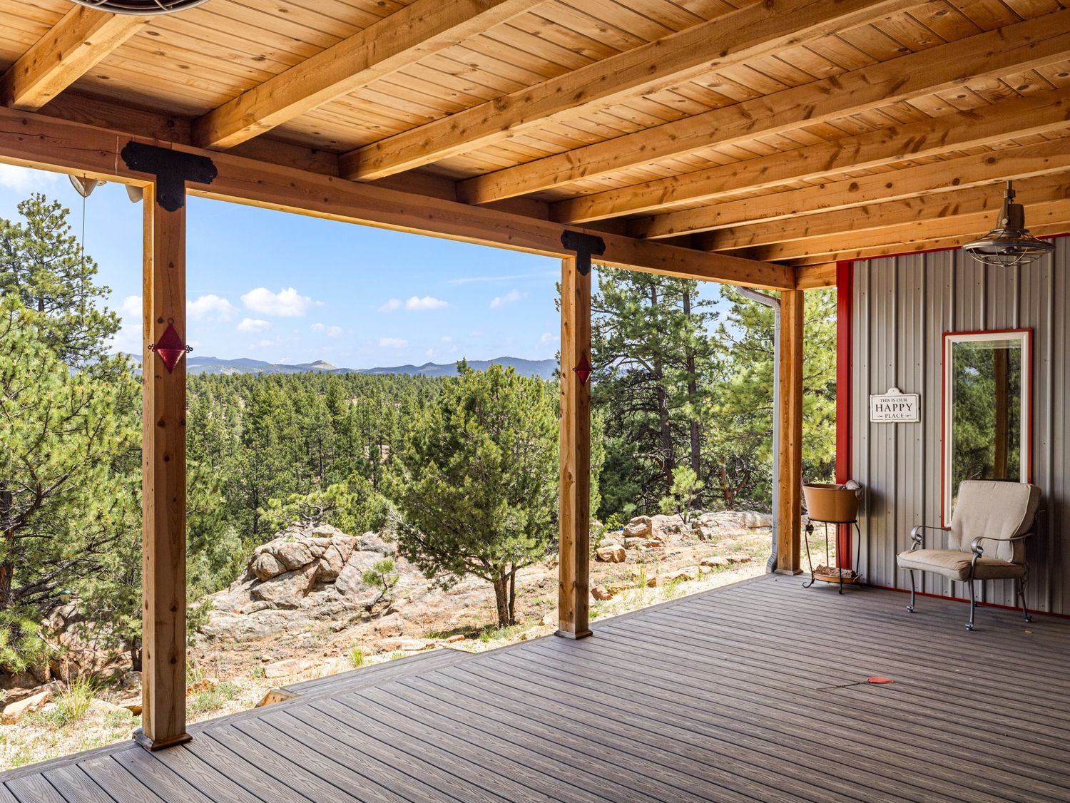 Covered wooden deck with mountain and forest views, exposed beam ceiling, and rustic outdoor living space.
