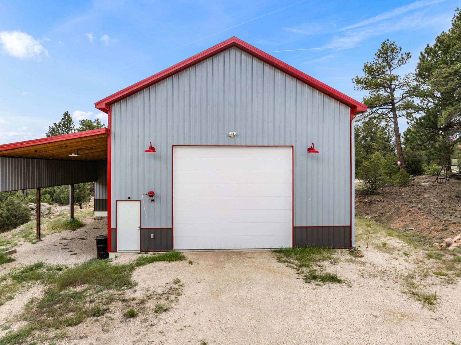 Detached metal pole barn garage with red trim, white door, and red barn lights.