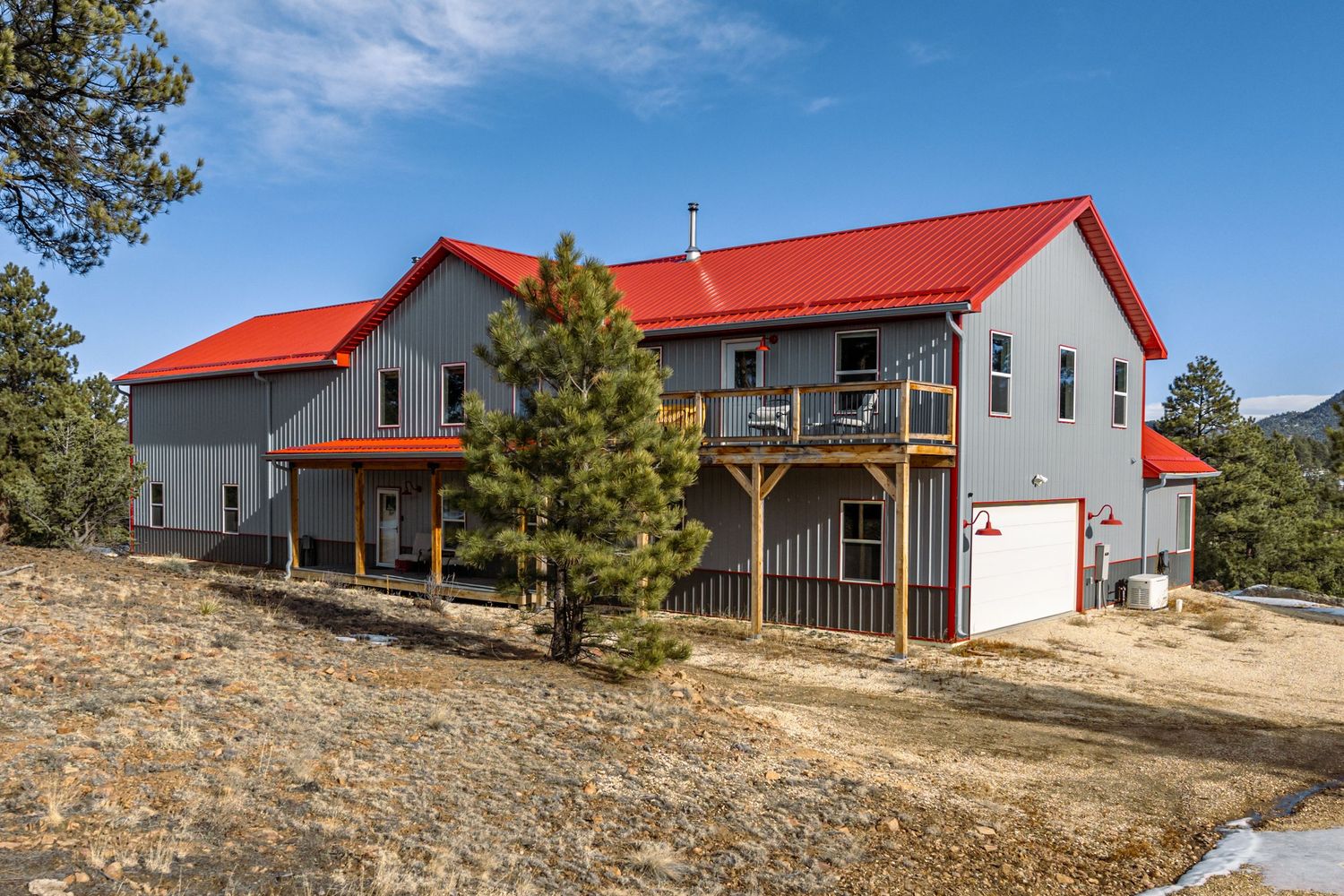Modern mountain residence with red roof and multi-level decks nestled among pine trees.