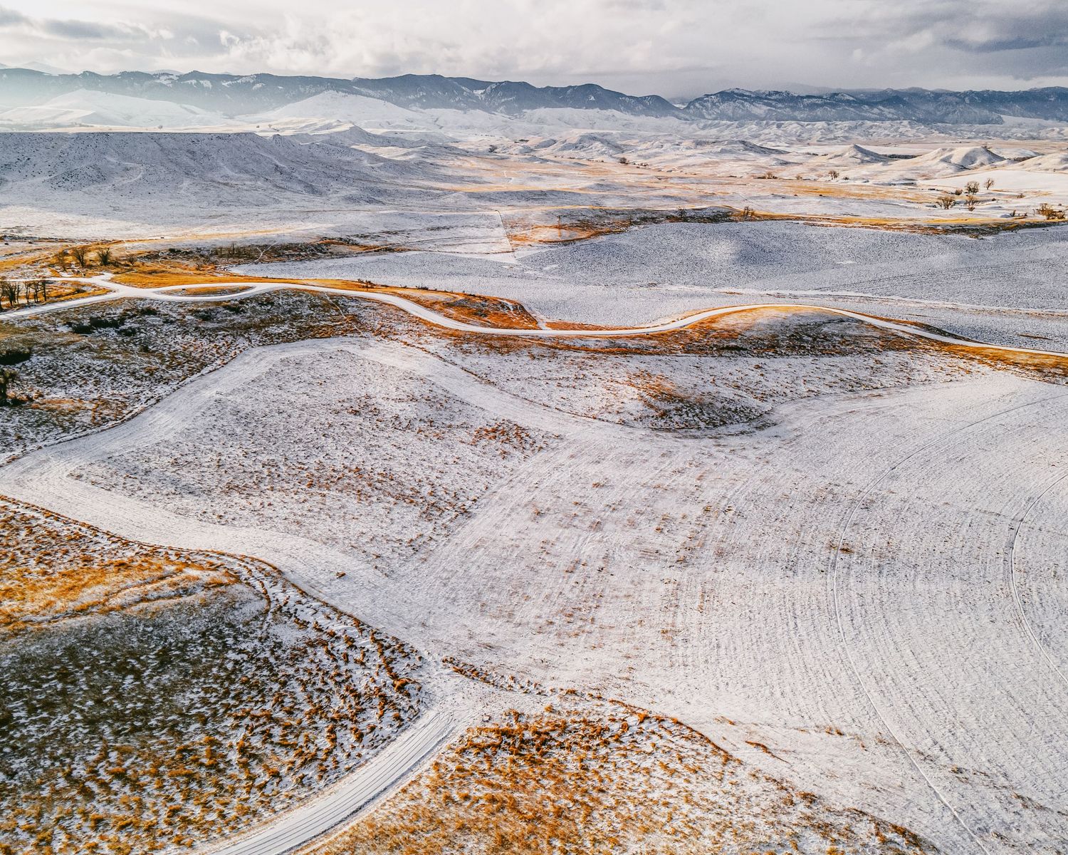 Aerial view of snowy mountain landscape with winding roads and rugged terrain.