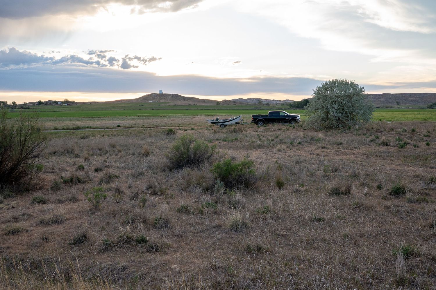 Black pickup truck parked in arid sagebrush terrain at sunset with distant buttes.