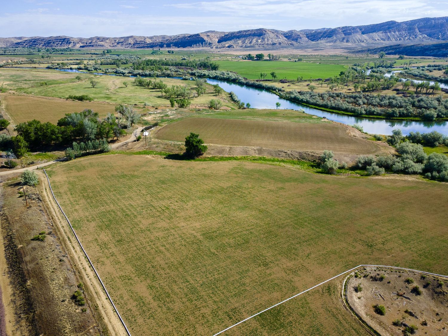 Aerial view of green farmland fields along a winding river with mountain backdrop.