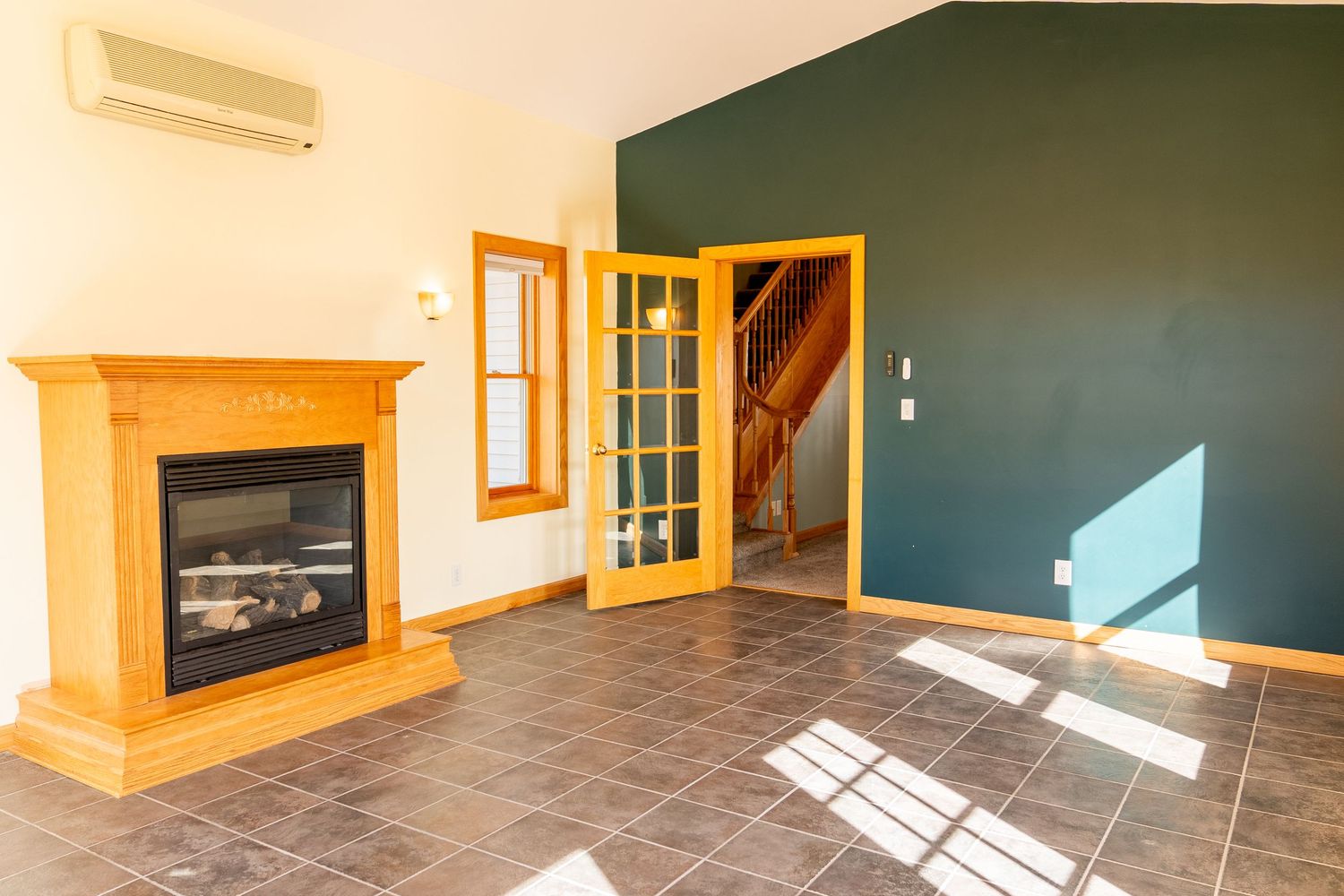 Bright living room with tile floors, wood-trimmed fireplace, green accent wall, French doors, and staircase.