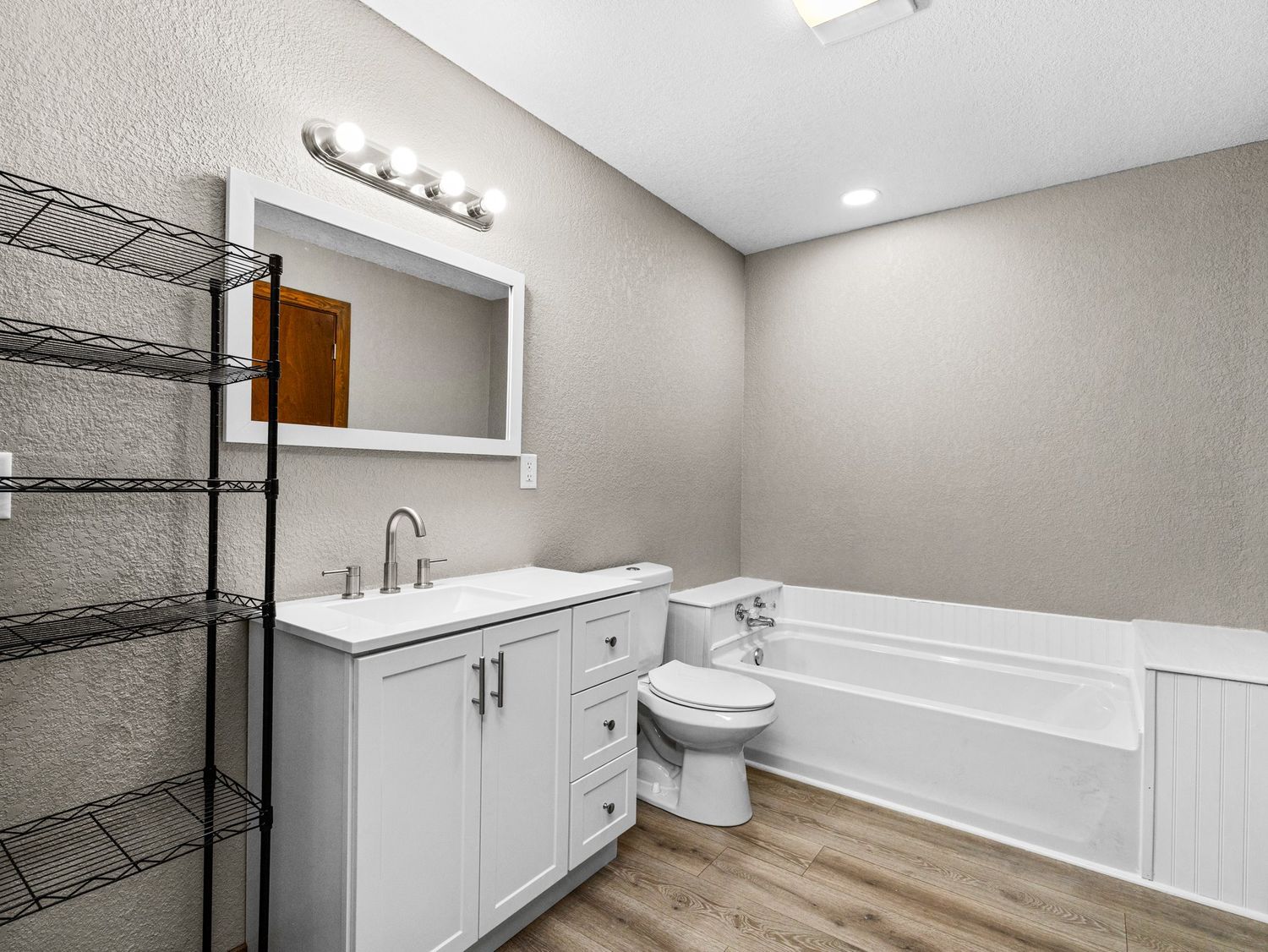 Full bathroom featuring white vanity, soaking tub, toilet, and wood-look flooring.