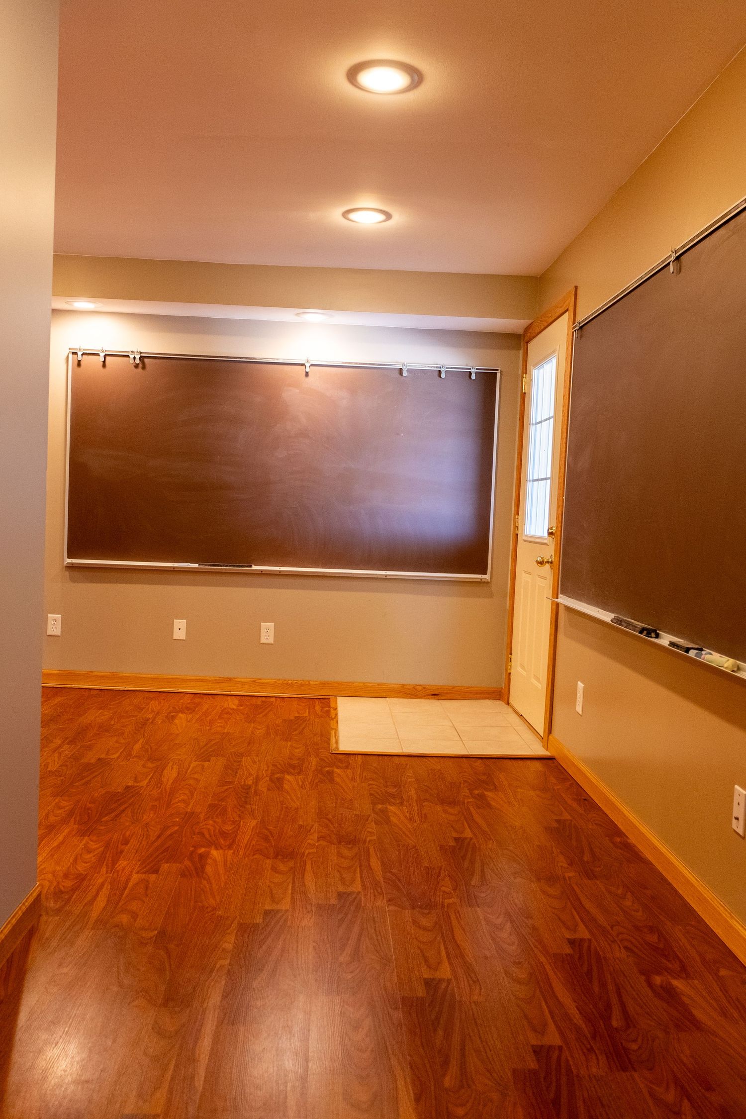 Empty room with hardwood floors, chalkboards on walls, recessed lighting, and a door with natural light.