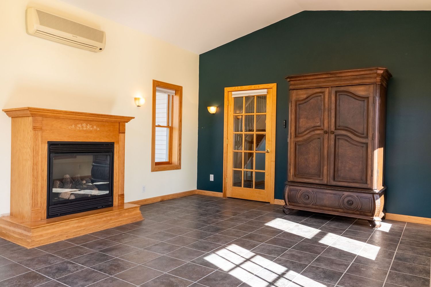 Living room with gas fireplace, dark green accent wall, tile floor, wooden armoire, and mini-split AC unit.
