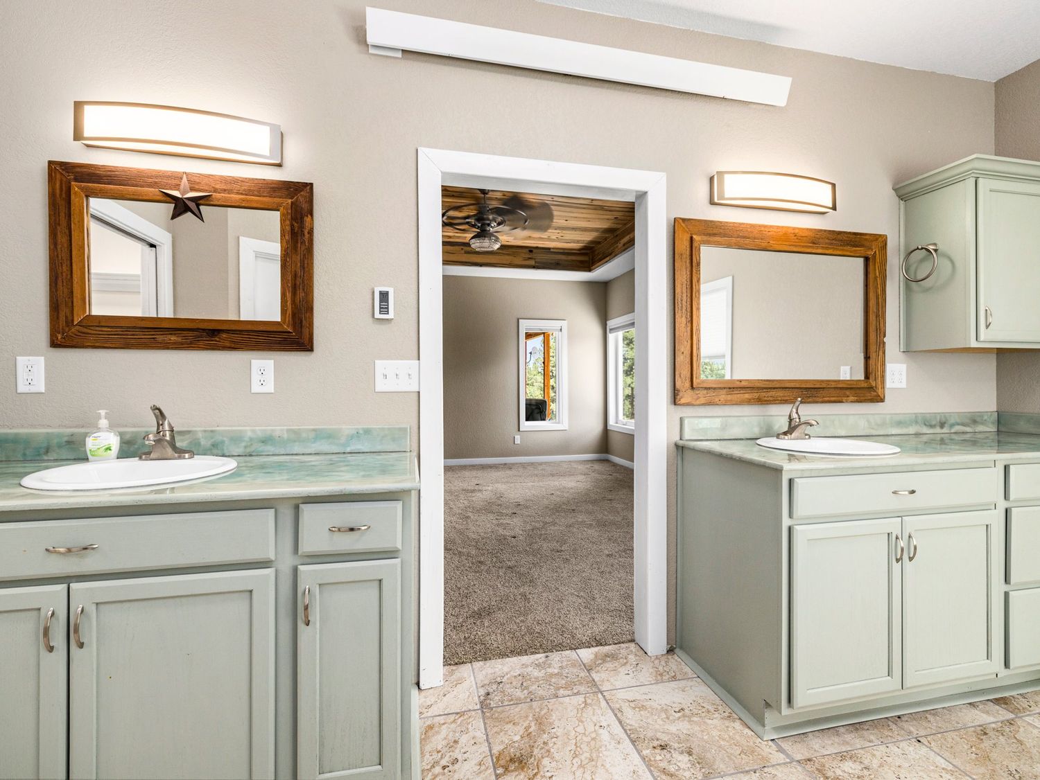 Spacious bathroom with sage green cabinets, dual sinks, wood-framed mirrors, and green countertops.