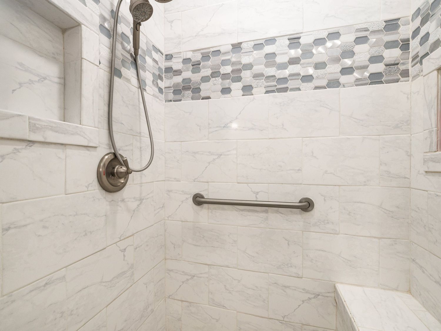 Elegant walk-in shower with marble tile walls, mosaic accent border, and brushed nickel fixtures.