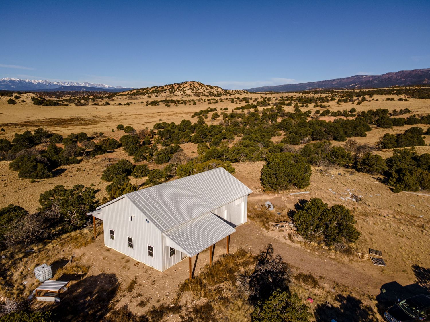 Aerial view of white structure situated among scattered juniper trees in high desert landscape.