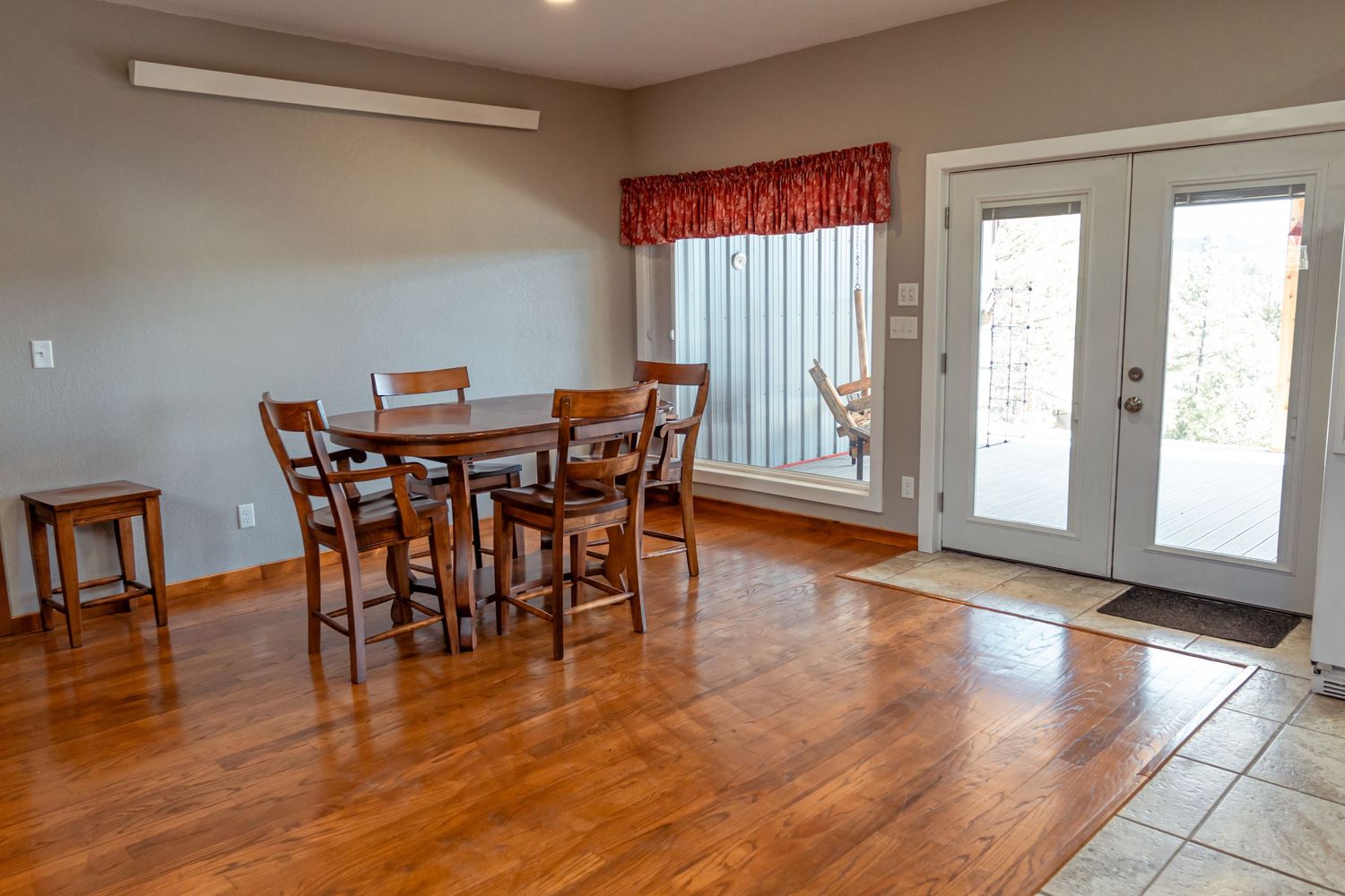 Dining area with wooden table and chairs next to French doors with red valance.
