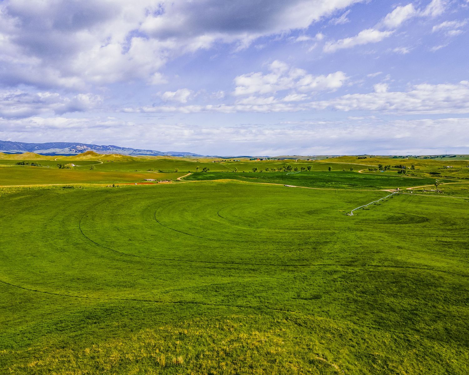 Rolling green hills stretch to the horizon under dramatic cloudy skies in this aerial view.