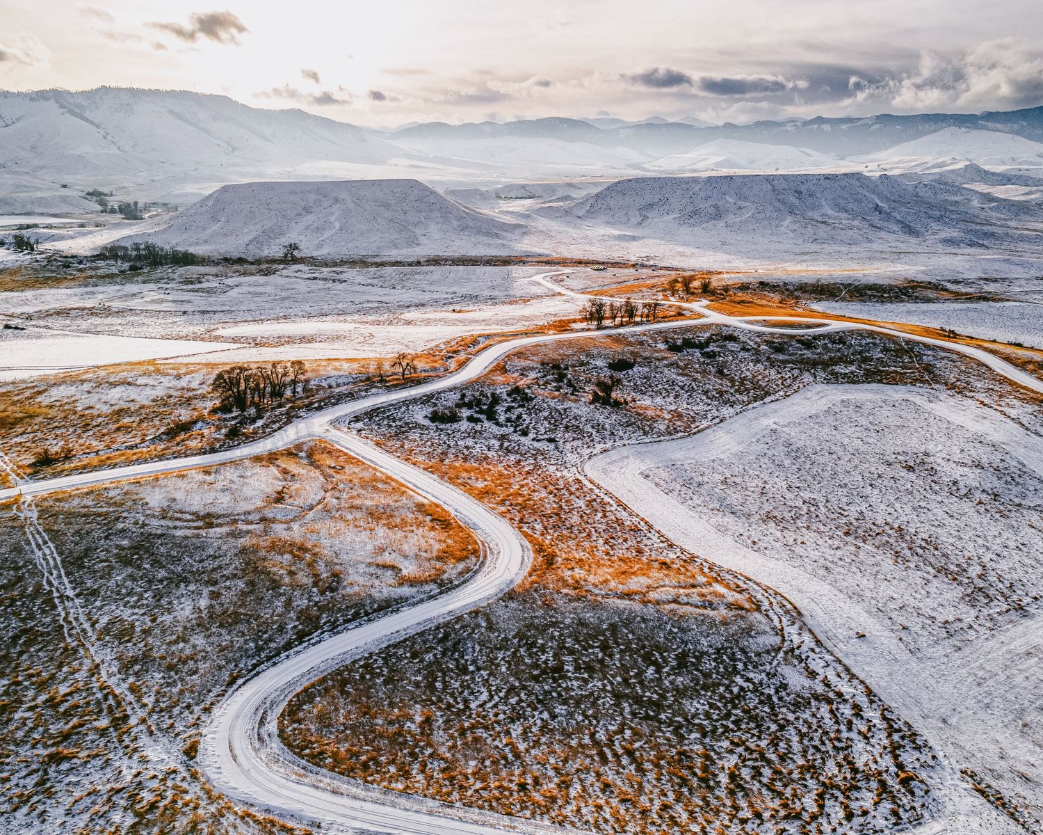 Winding mountain road cuts through snow-covered terrain at sunset.
